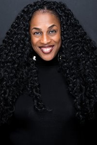 Photo of Robyne Walker Murphy. She has a wide smile, long curly black hair, brown skin, and wears reddish-brown lipstick, silver earrings, and black top. The background is grey.