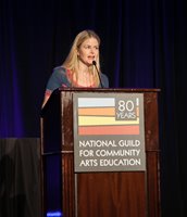 Photo of Heather on stage at the Conference for Community Arts Education, with a sign on the podium with the Guild logo that says "80 Years"