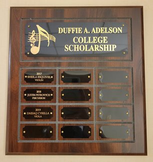 A plaque that reads "Duffie A. Adelson College Scholarship" with an image of music notes, and the names of scholarship recipients listed at the bottom.