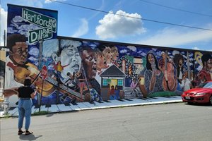 Rangsey stands in front of a large music-themed mural on the outside of the Atlanta Music Project building.