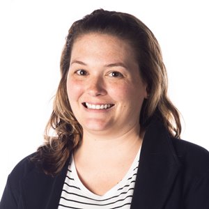 Erin Dunn headshot. Erin smiles into the camera, with a white background behind her. She has light skin and light brown, straight hair falling to her shoulders, and wears a white top with dark horizontal stripes and a navy blue blazer.