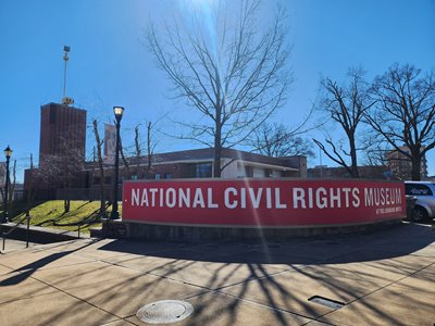 The exterior of the National Civil Rights Museum, with a red and white sign with the msueum's name in the foreground, and a clear blue sky in the background.