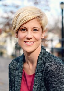 A headshot of Dancing Classrooms executive director Nancy Kleaver. She has short blonde hair and fair skin, and is wearing a pink blouse under a dark gray jacket.